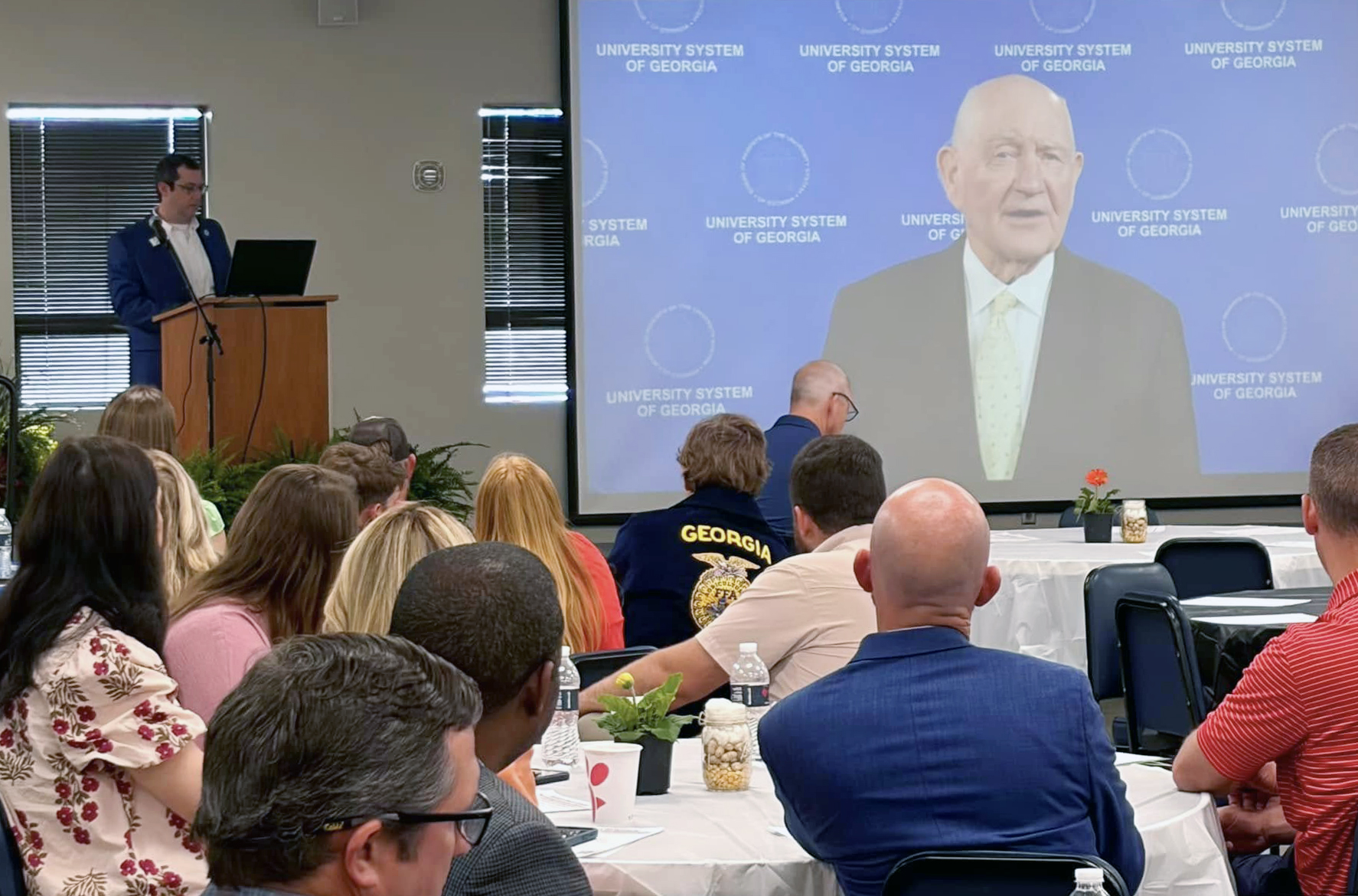 A group of people sitting and watching a speaker on a screen